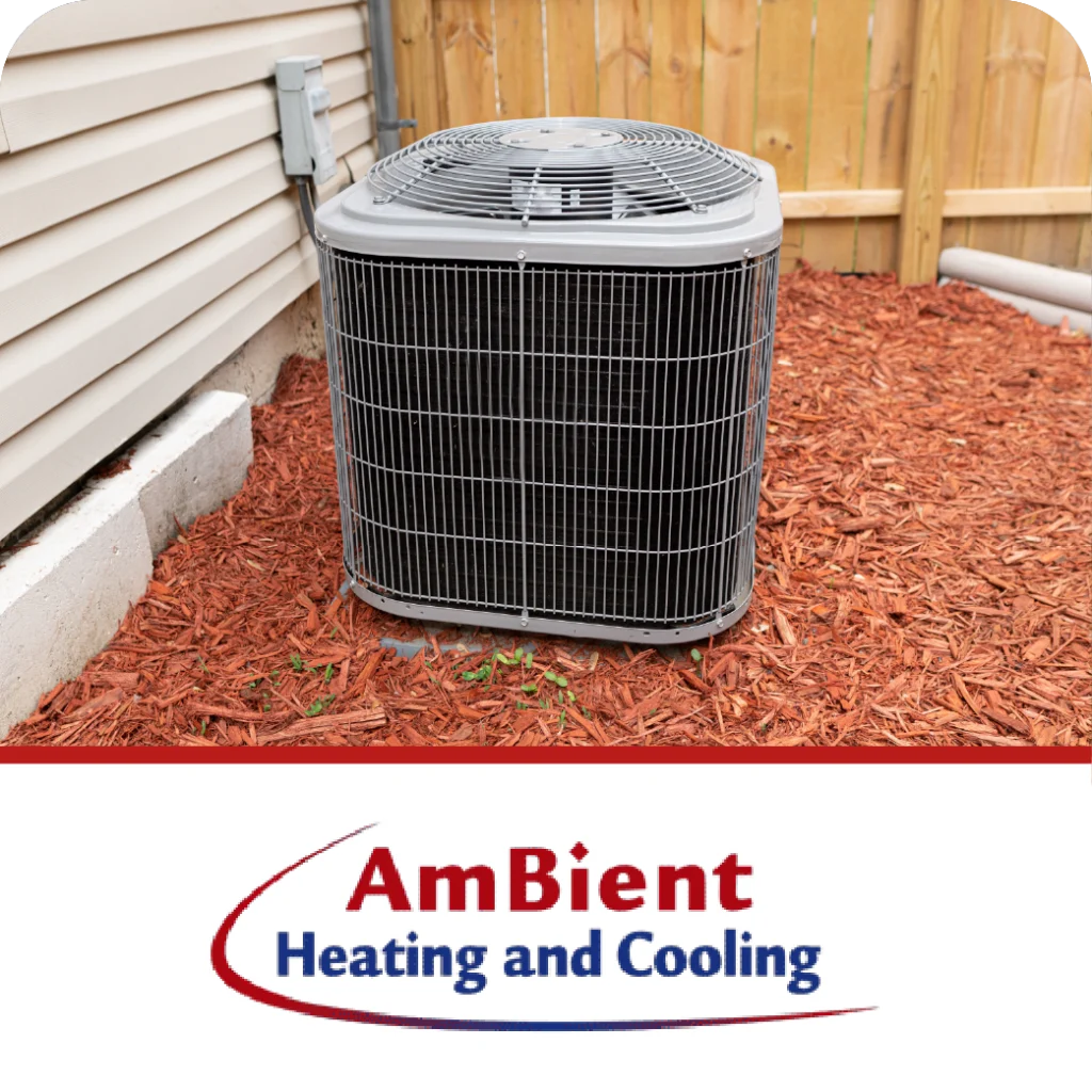 An outdoor AC unit sits on mulch next to a house, with the "AmBient Heating and Cooling" logo